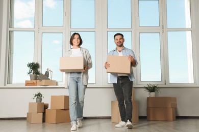 Happy couple with moving boxes near big window in new apartment