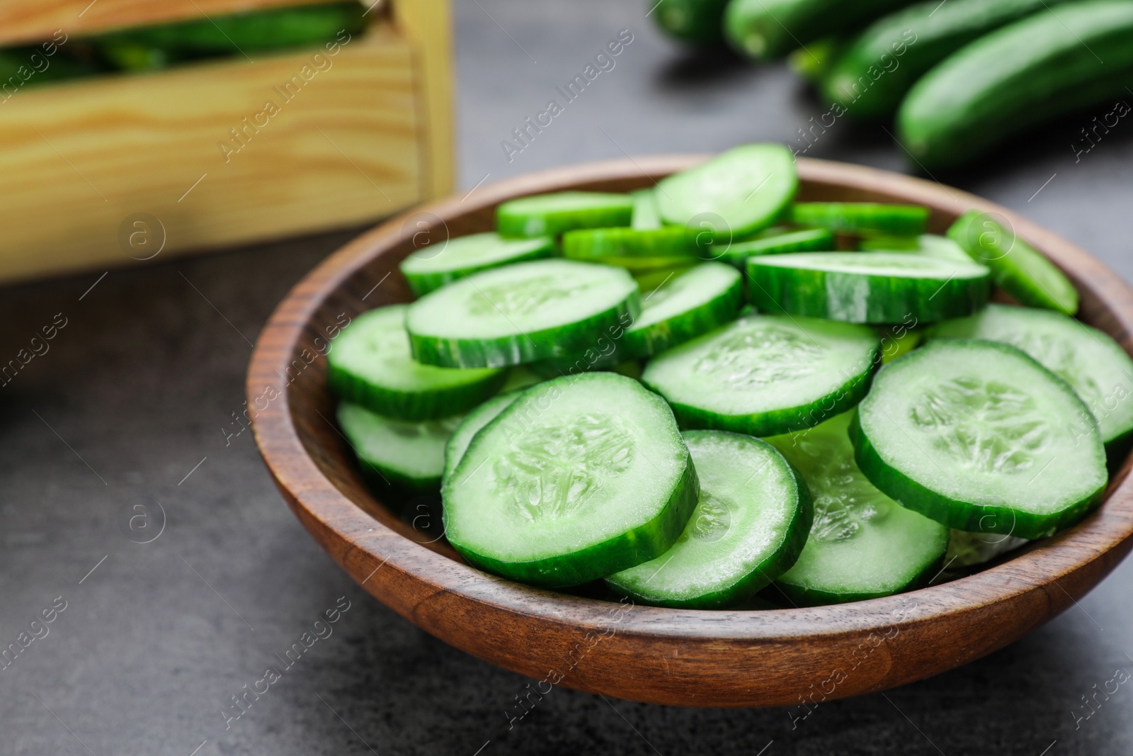 Photo of Slices of fresh ripe cucumber in bowl on grey table, closeup