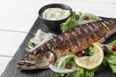 Slate plate with delicious grilled fish and sauce on table, closeup