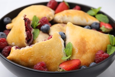 Bowl with delicious samosas, berries and mint leaves on table, closeup