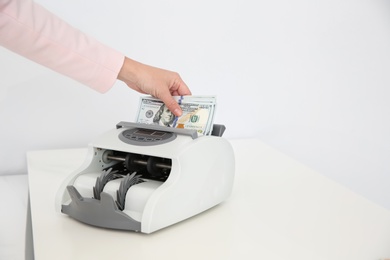 Woman putting money into counting machine on table, closeup. Space for text