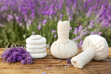 Photo of Spa stones, fresh lavender flowers and herbal bags on wooden table outdoors, closeup