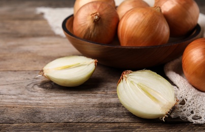 Photo of Cut and whole onions on wooden table, space for text