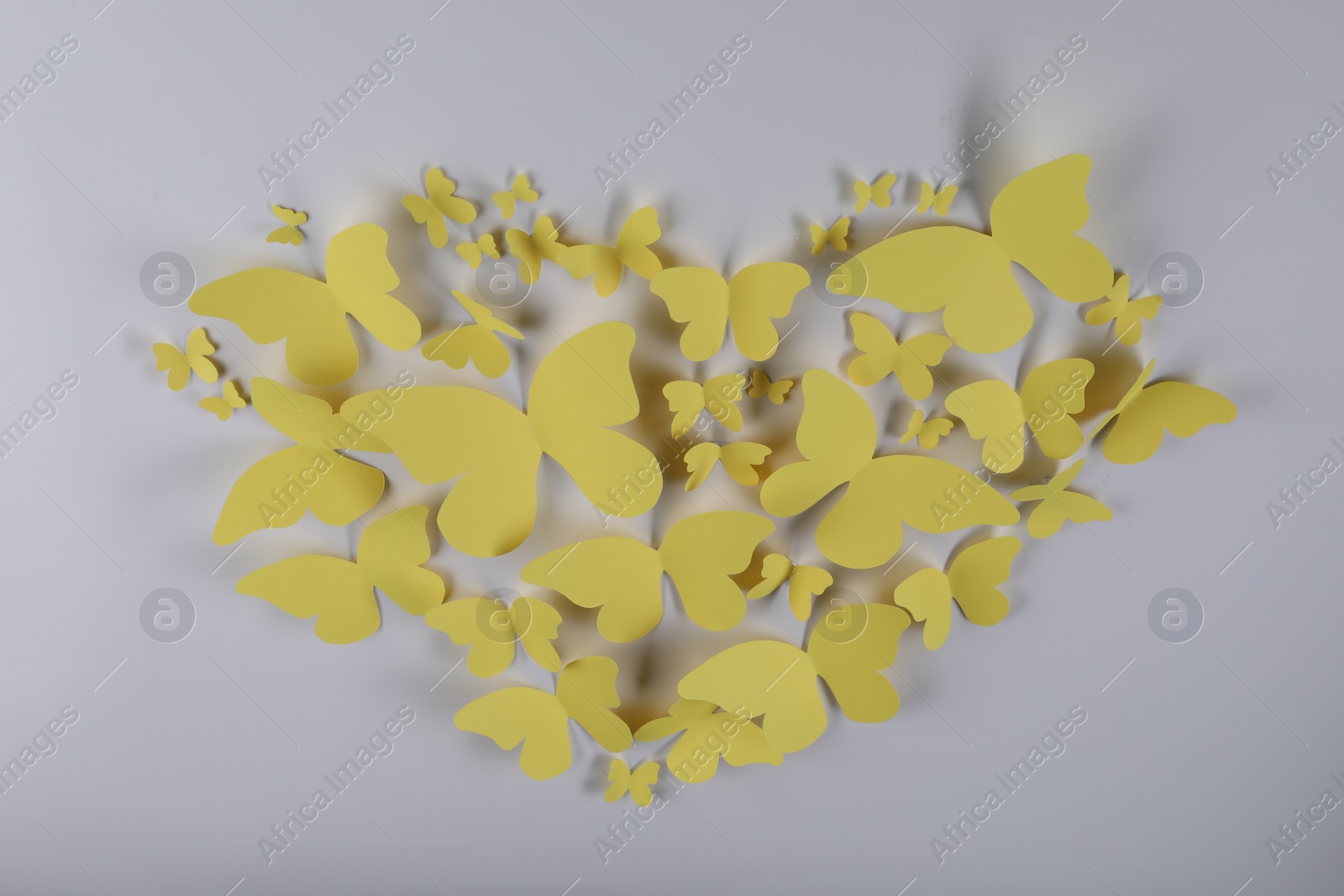 Photo of Heart shape made of yellow paper butterflies on light grey background