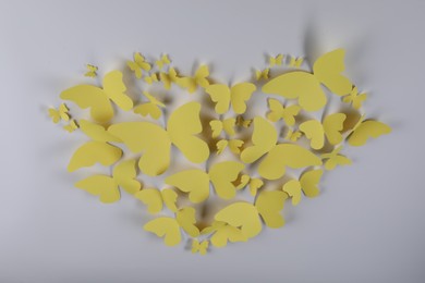 Photo of Heart shape made of yellow paper butterflies on light grey background