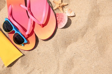 Flip flops and other beach accessories on sand, flat lay. Space for text