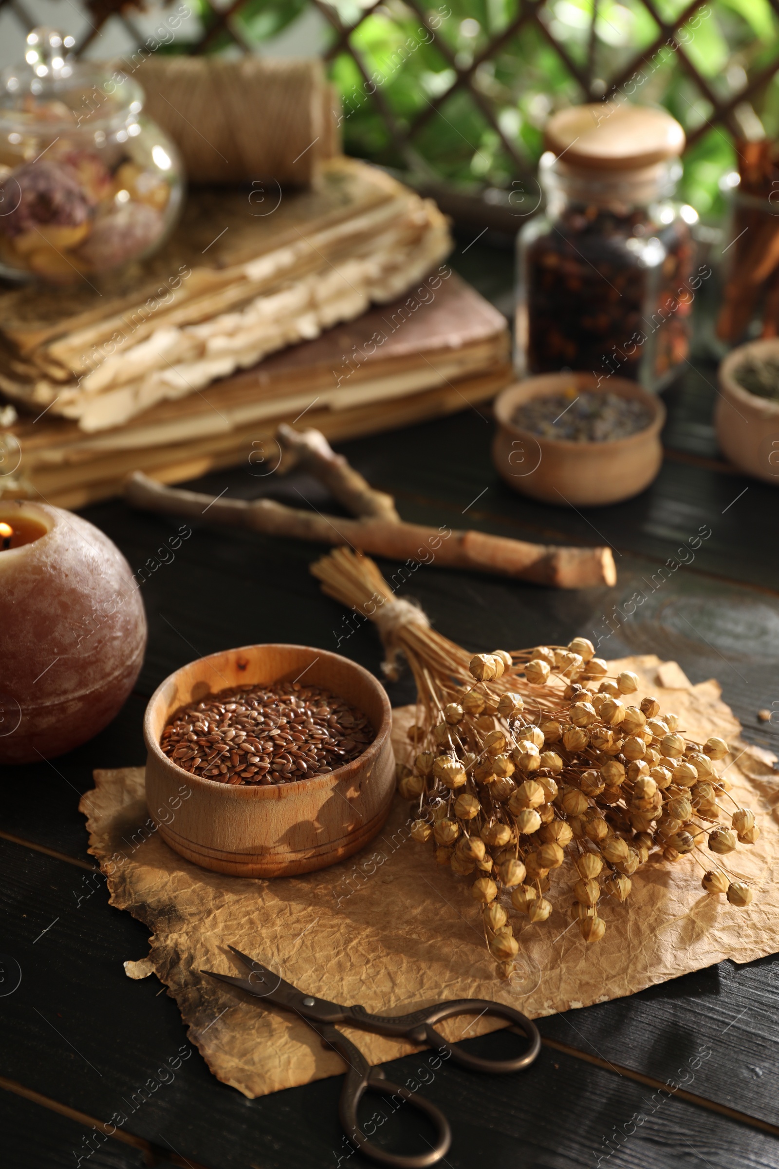 Photo of Flax seeds with dry flowers and scissors on black wooden table indoors