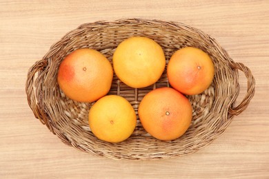 Photo of Wicker basket with fresh ripe grapefruits on wooden table, top view