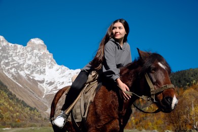 Photo of Young woman riding horse in mountains on sunny day. Beautiful pet