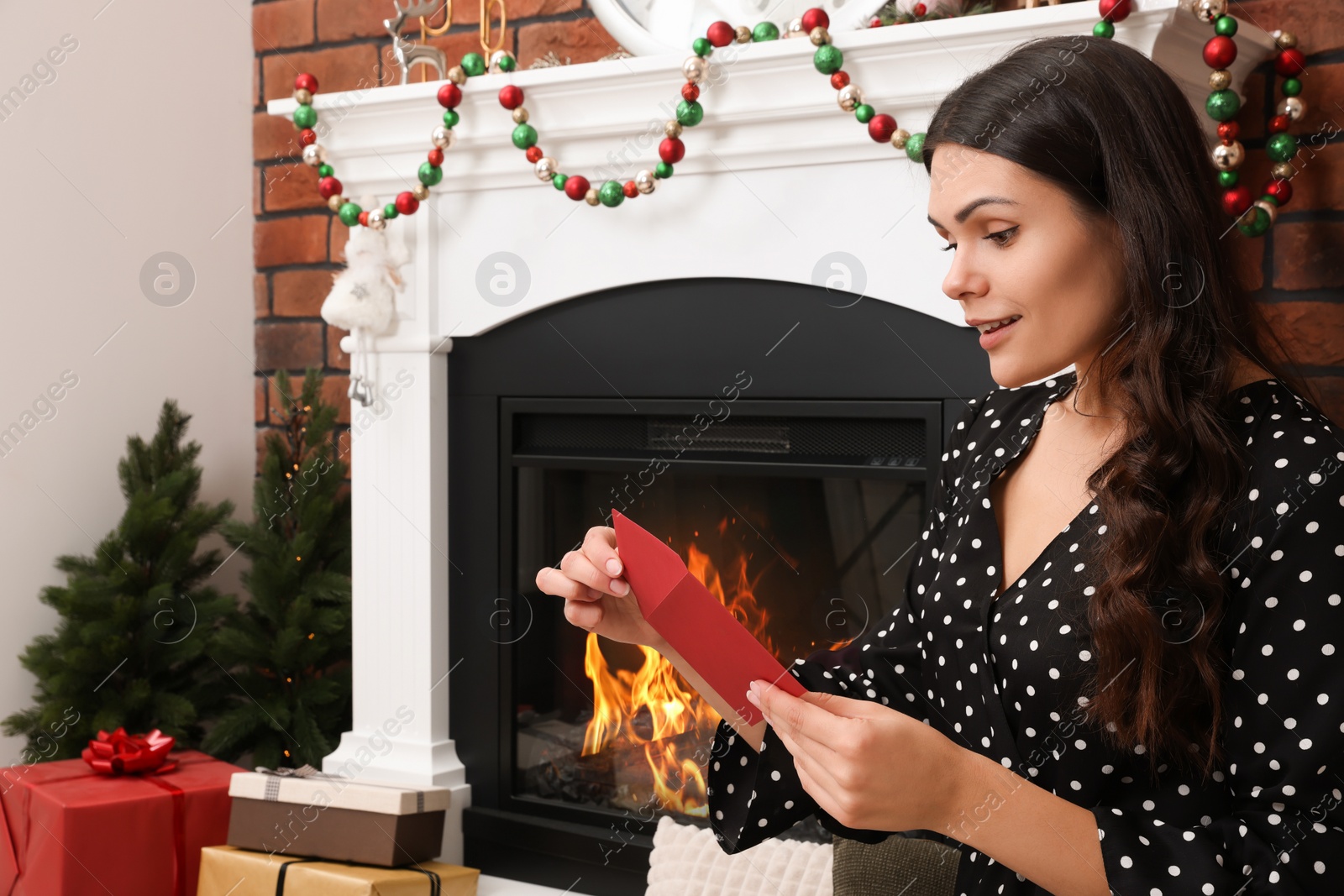 Photo of Young woman with greeting card sitting near fireplace indoors