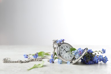 Photo of Beautiful blue forget-me-not flowers with pocket watch on light stone table. Space for text