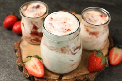 Photo of Tasty yoghurt with jam and strawberries on grey textured table, closeup