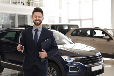 Salesman with key and clipboard in car salon