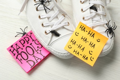 Photo of Shoes with fake spiders, bugs and Happy Fools' Day note on white wooden table, closeup