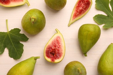 Cut and whole green figs with leaves on white wooden table, flat lay