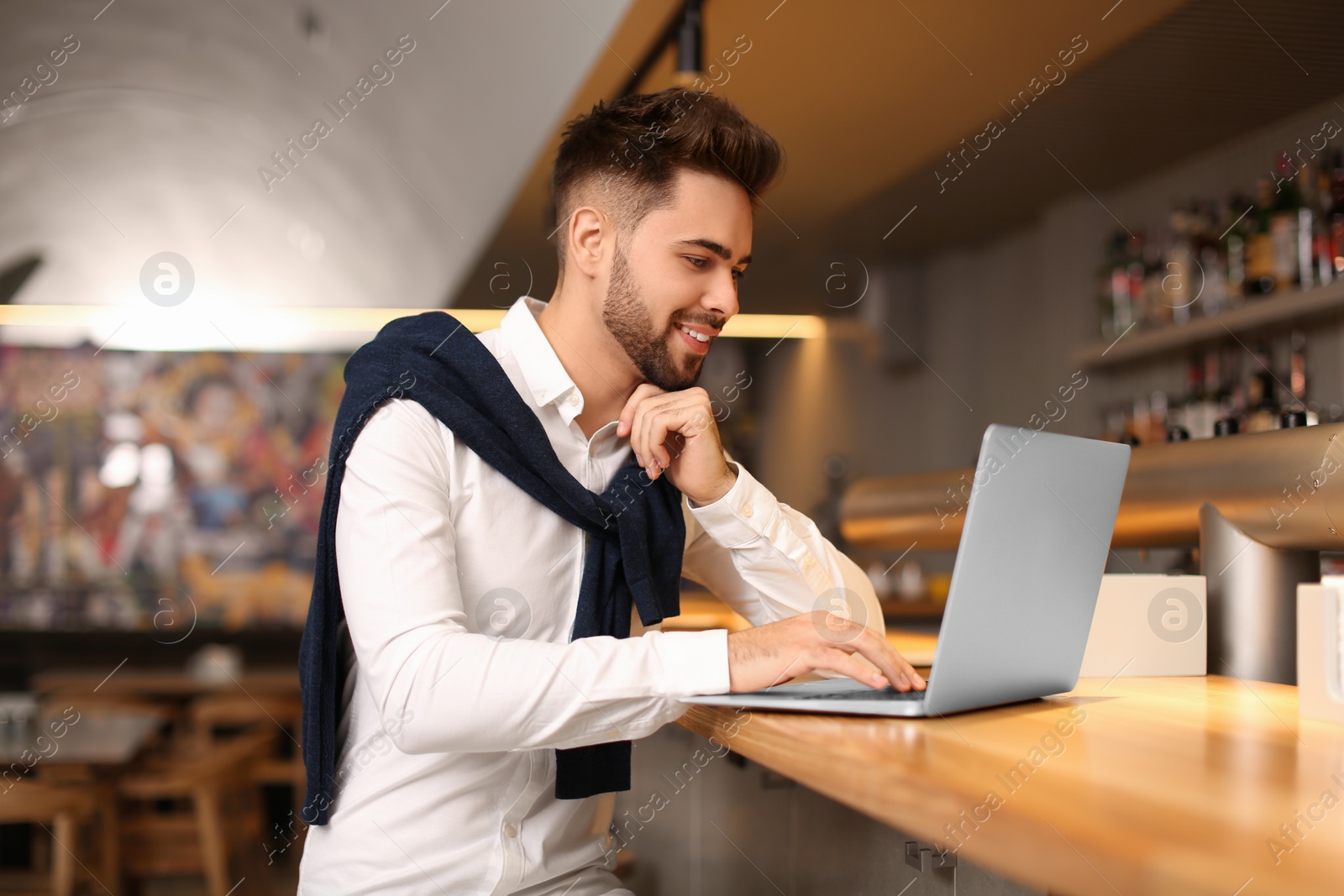 Photo of Young male business owner working with laptop at counter in his cafe