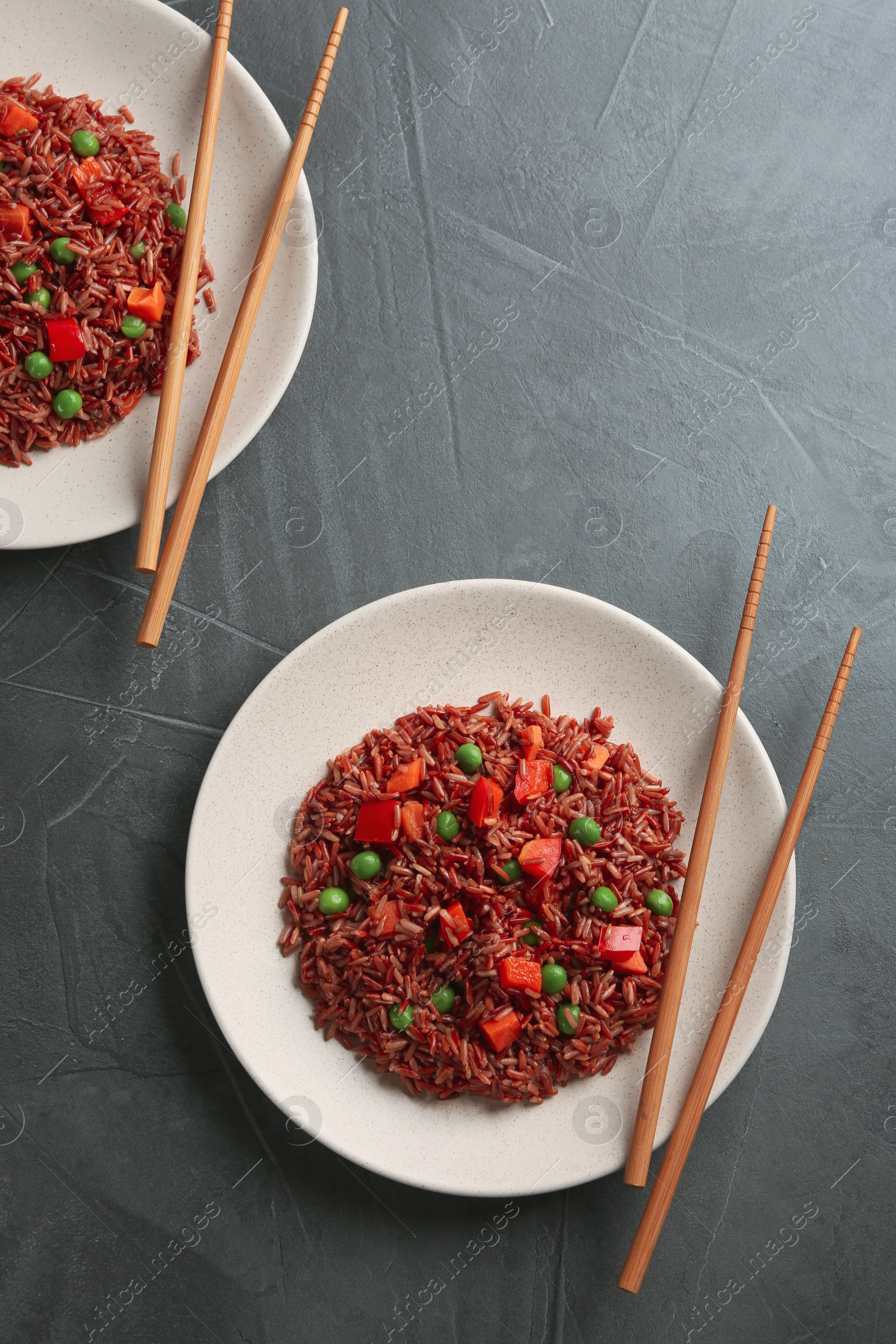 Photo of Tasty brown rice with vegetables on dark grey table, flat lay