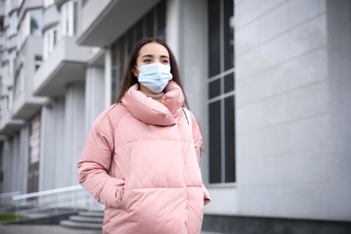 Photo of Young woman in medical face mask walking outdoors. Personal protection during COVID-19 pandemic