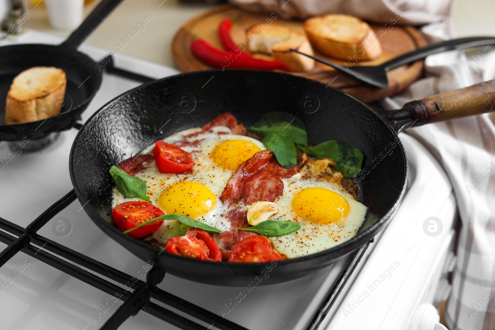 Photo of Delicious fried eggs with bacon and tomatoes in pan on stove