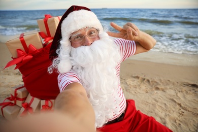 Santa Claus with bag of presents taking selfie on beach. Christmas vacation