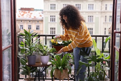 Beautiful young woman spraying potted houseplants with water on balcony