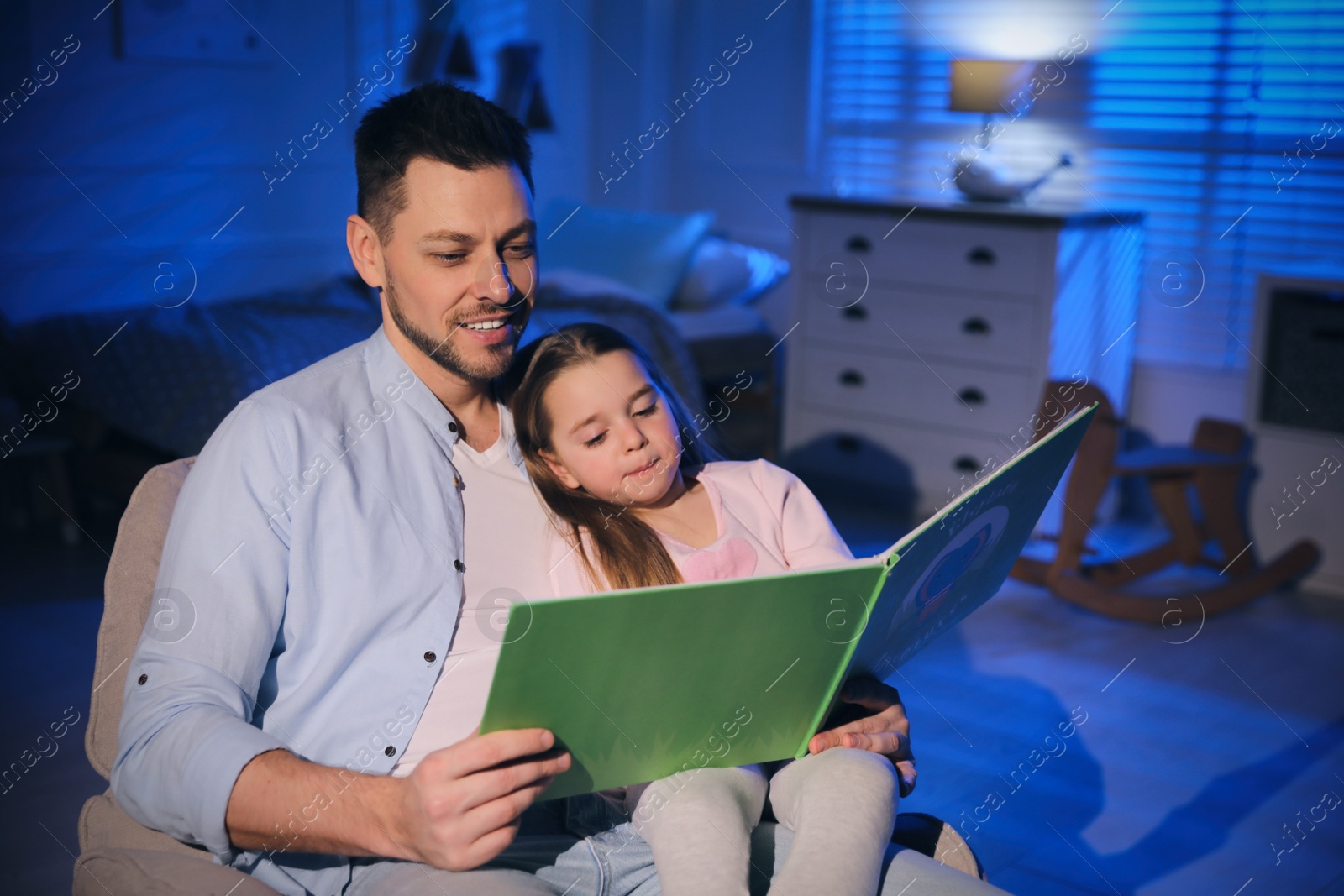 Photo of Father reading bedtime story to his daughter at home