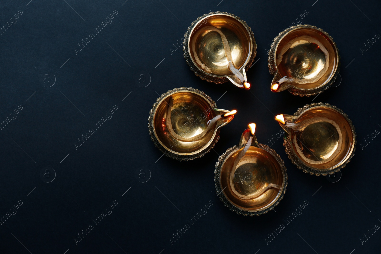 Photo of Lit diyas on dark background, flat lay with space for text. Diwali lamps