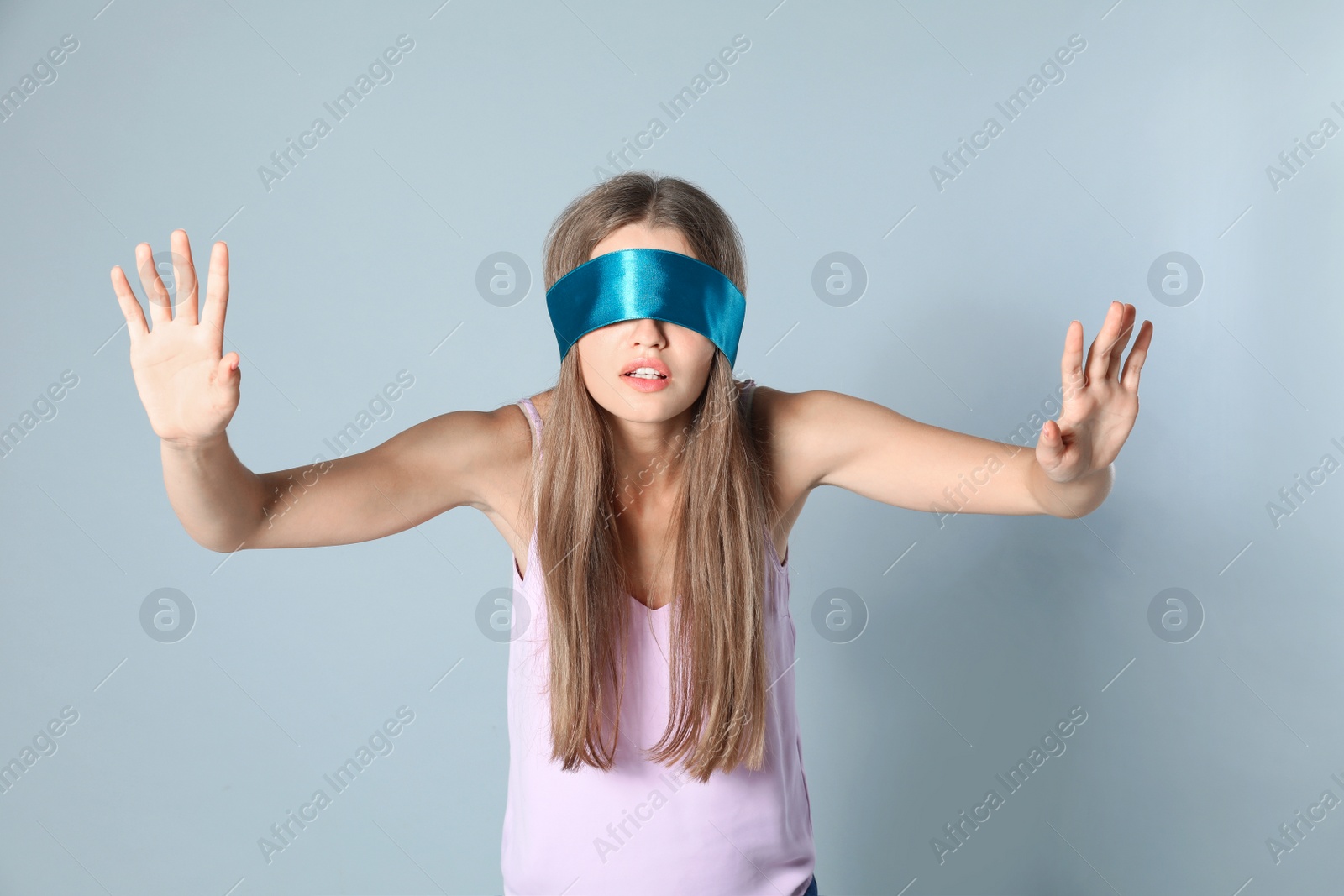 Photo of Young woman with light blue blindfold on grey background