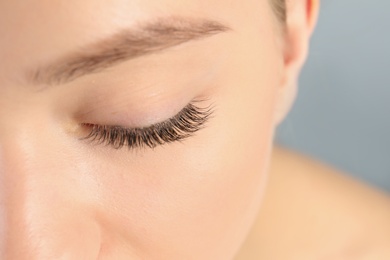 Young woman with beautiful long eyelashes on gray background, closeup. Extension procedure