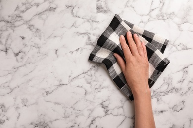 Photo of Woman wiping marble table with kitchen towel, top view. Space for text