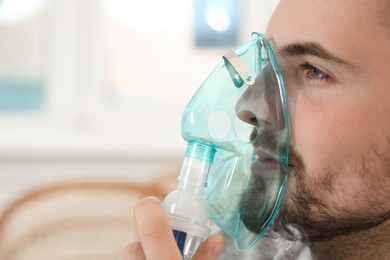 Photo of Sick man using inhalation nebulizer indoors, closeup. Space for text