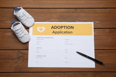 Photo of Adoption application, baby shoes and pen on wooden table, flat lay