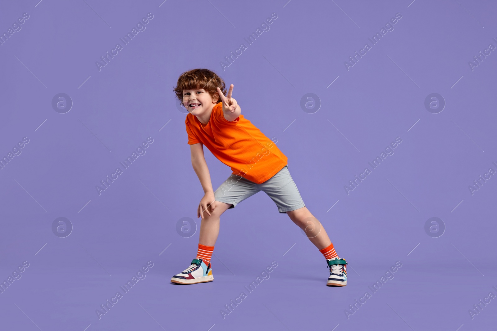 Photo of Happy little boy dancing on violet background