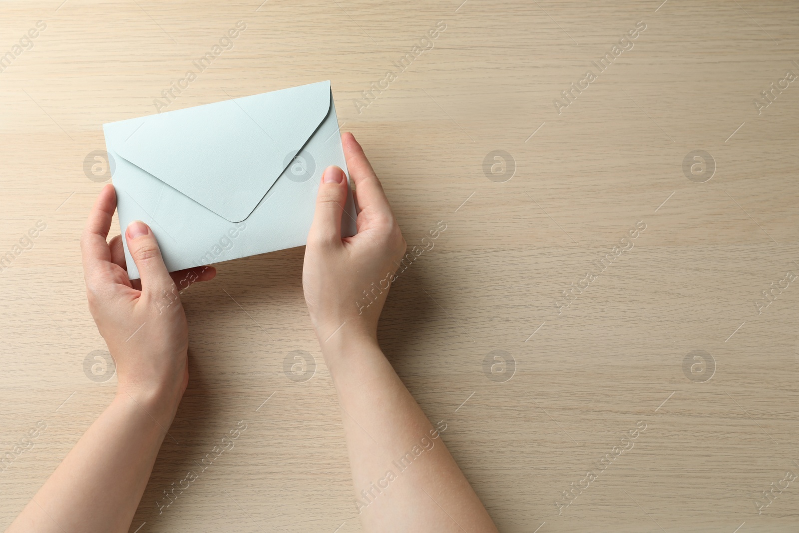 Photo of Woman with white paper envelope at wooden table, top view. Space for text