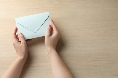 Woman with white paper envelope at wooden table, top view. Space for text