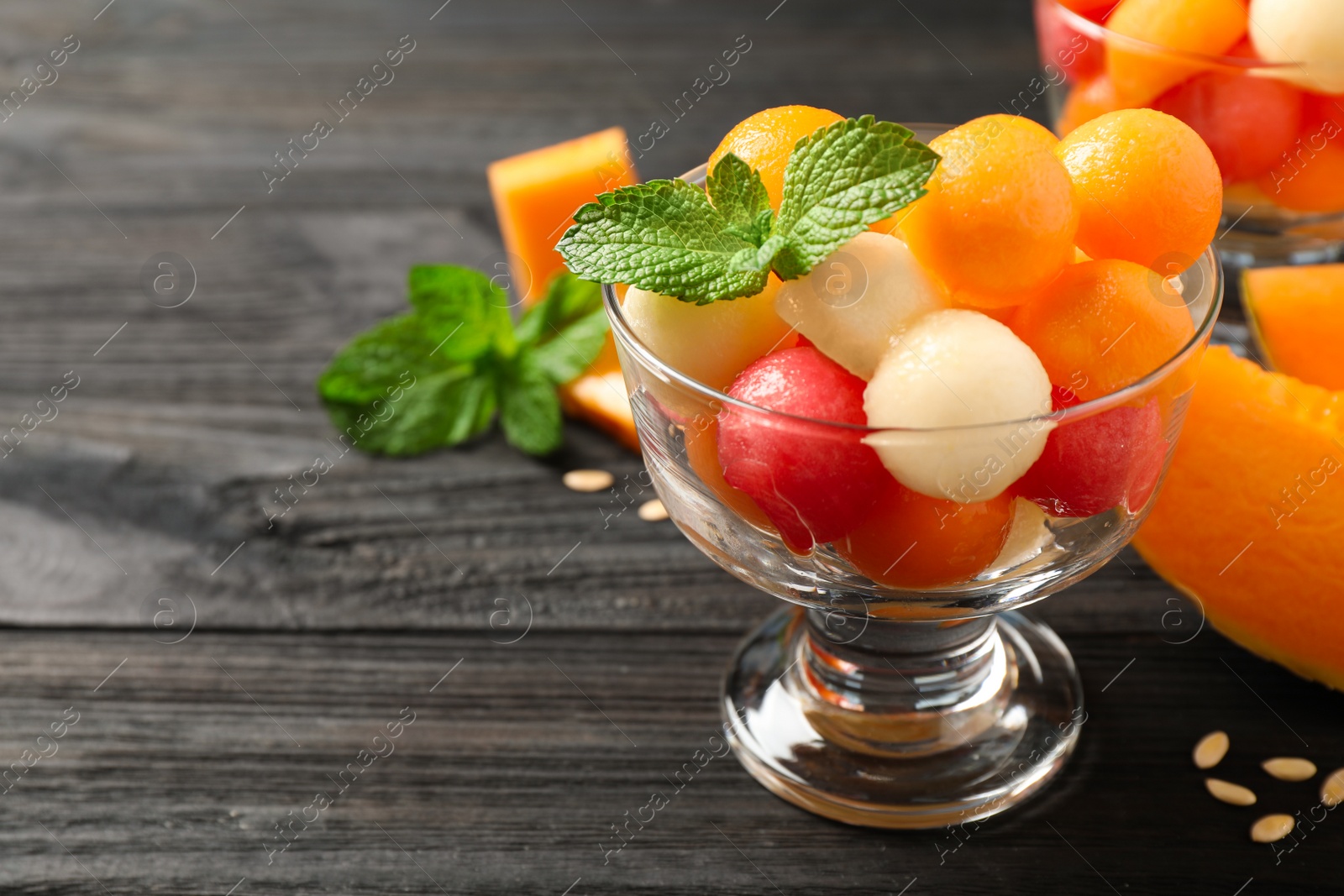 Photo of Melon and watermelon balls with mint in dessert bowl on black wooden table. Space for text