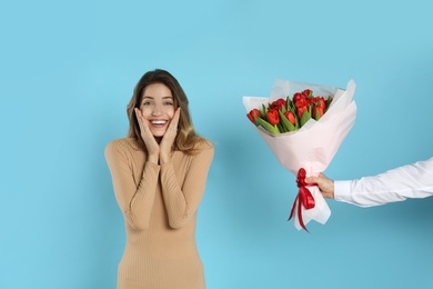 Happy woman receiving red tulip bouquet from man on light blue background. 8th of March celebration