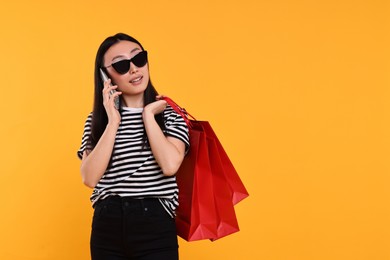 Photo of Beautiful woman with shopping bags talking by smartphone on yellow background. Space for text
