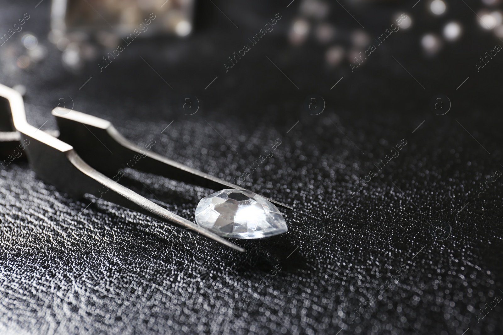 Photo of Jewel and tweezers on black leather surface