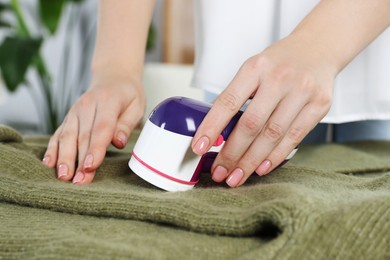 Photo of Woman cleaning clothes with fabric shaver indoors, closeup