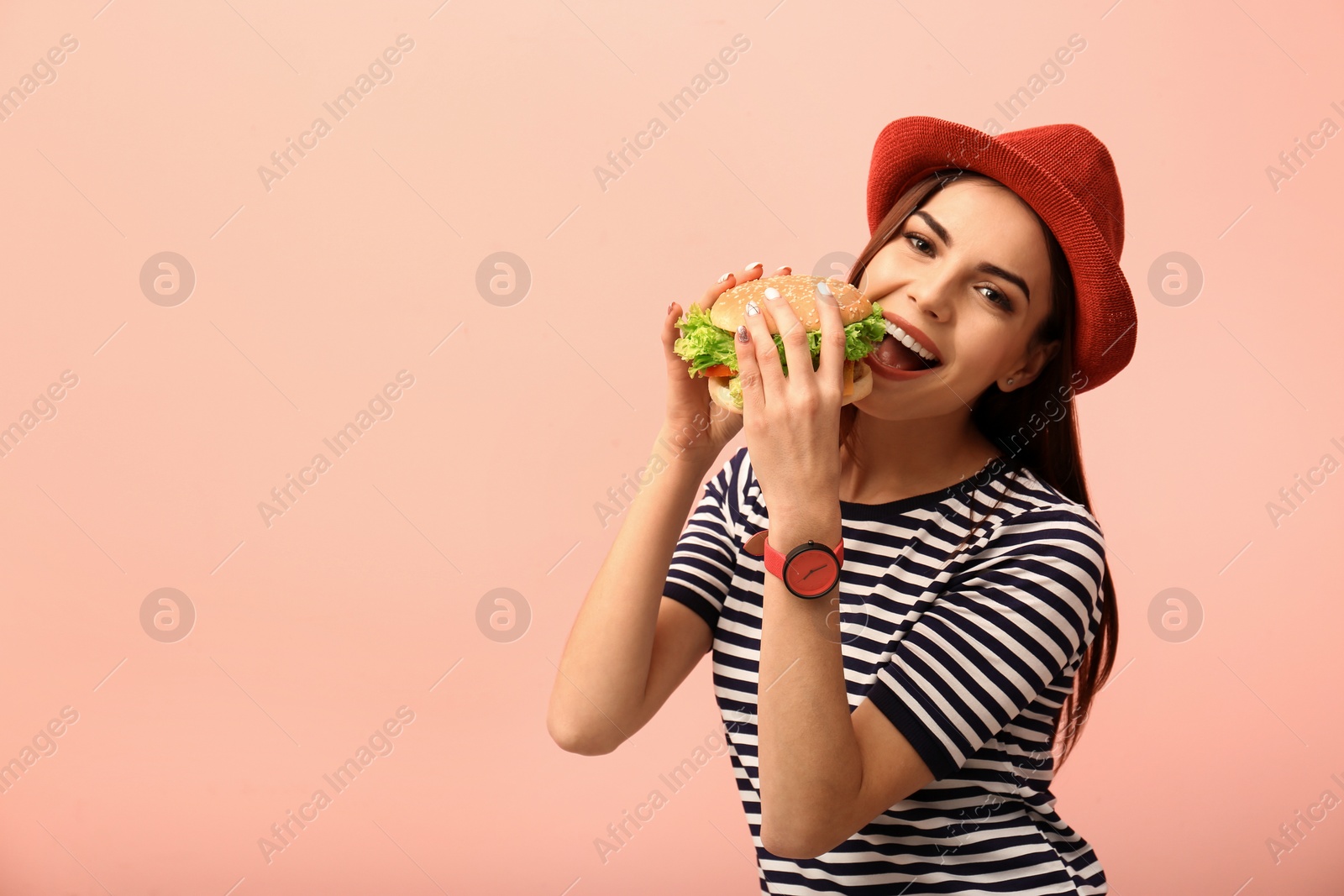 Photo of Young woman eating tasty burger on color background. Space for text