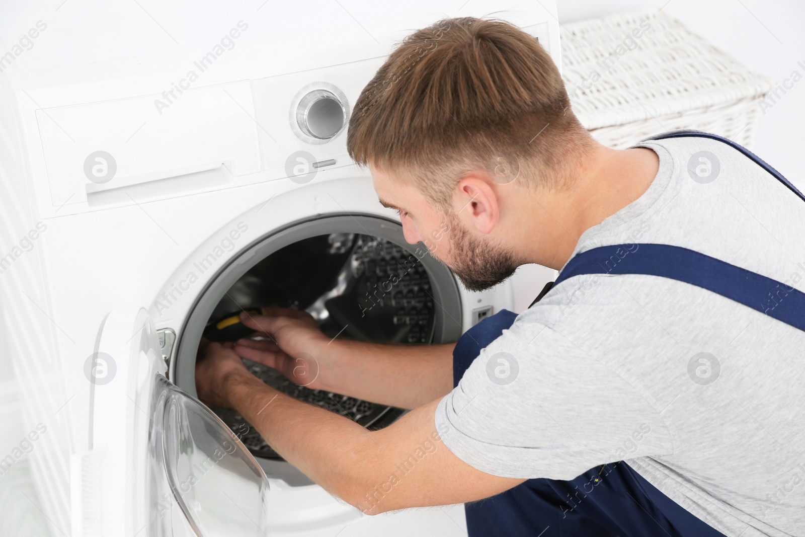 Photo of Young plumber fixing washing machine in bathroom