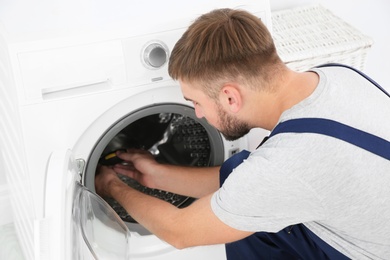 Young plumber fixing washing machine in bathroom