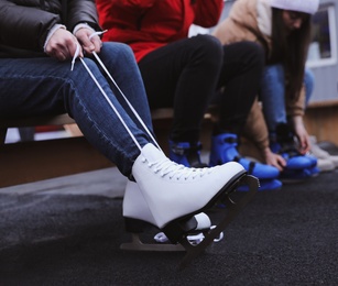Young woman wearing white ice skates on bench outdoors, closeup