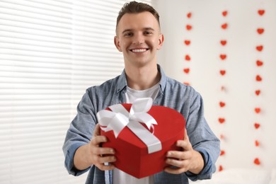 Photo of Handsome young man with gift box indoors, view from camera. Valentine's day celebration in long distance relationship