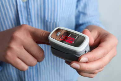 Woman using modern fingertip pulse oximeter on light background, closeup