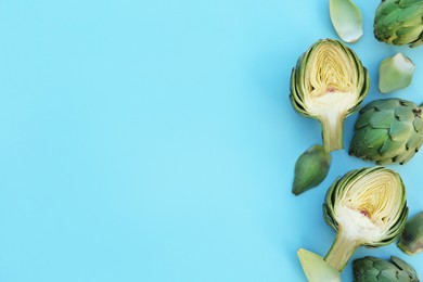 Photo of Whole and cut fresh raw artichokes on light blue background, flat lay. Space for text