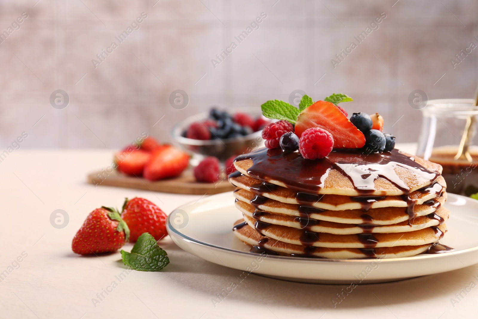 Photo of Stack of tasty pancakes with fresh berries, chocolate sauce and mint on white table. Space for text