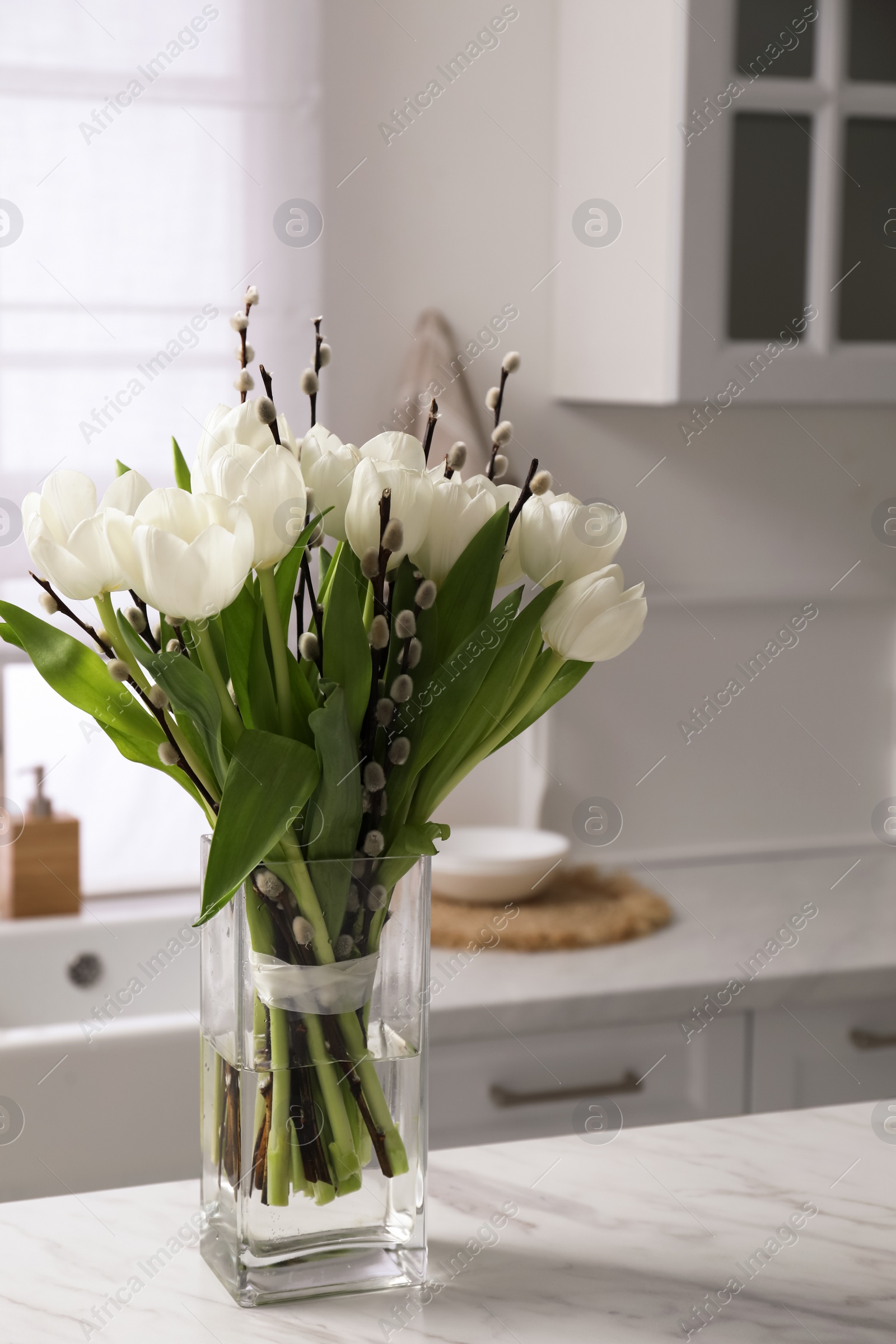 Photo of Beautiful bouquet of willow branches and tulips in vase on white table indoors, space for text