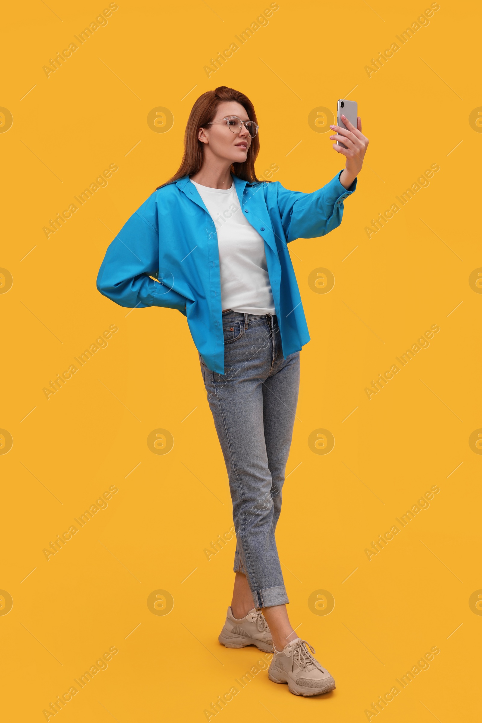 Photo of Beautiful woman in eyeglasses taking selfie on orange background